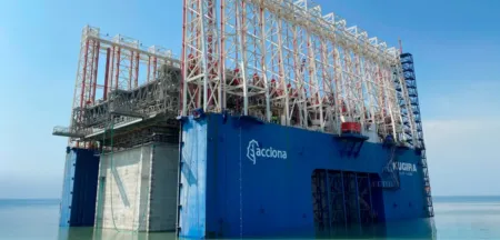 Offshore drilling platform with a blue base and white lattice framework rising from calm sea water under a clear blue sky.