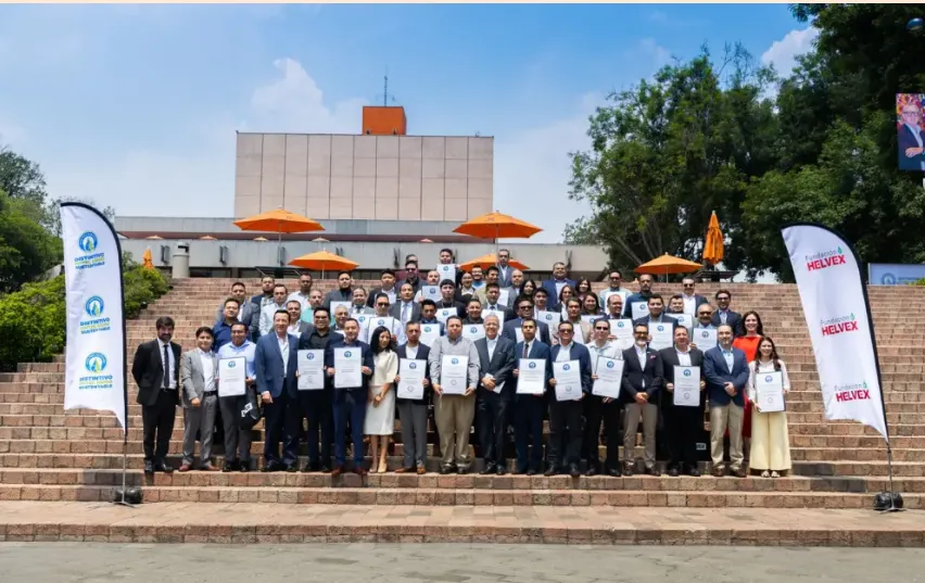 Group of professionals on stepped podium holding certificates at an outdoor ceremony with orange umbrellas and banners on both sides.