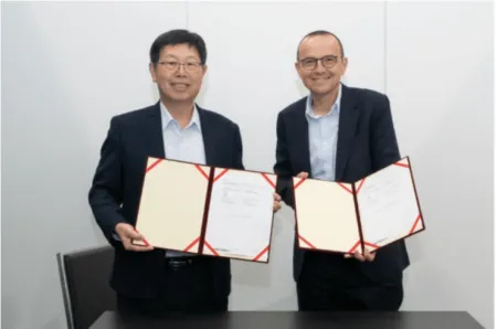 Two men in dark suits stand beside a table, holding open folders with signed documents from a formal agreement ceremony