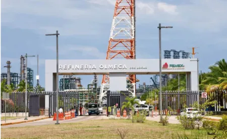 Entrance to Refinería Olmeca Dos Bocas Pemex with gate, security, and a tall orange‑and‑white lattice tower in the background.