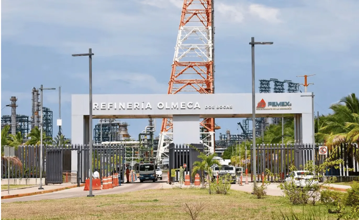 Entrance to Refinería Olmeca Dos Bocas Pemex with gate, security, and a tall orange‑and‑white lattice tower in the background.
