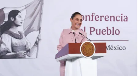 Woman in a pink suit giving a speech at a lectern with the Mexican seal, conference backdrop reading 'Conferencia'.