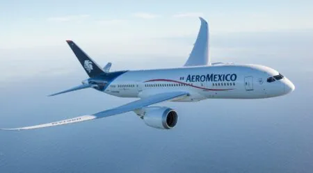 Aeromexico aircraft in level flight over the ocean, white fuselage with blue tail and red swoosh logo on the side of the plane's body.