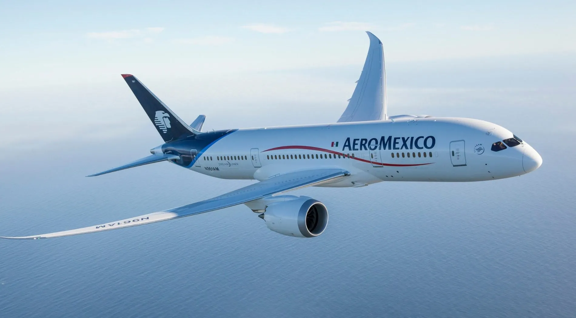 Aeromexico aircraft in level flight over the ocean, white fuselage with blue tail and red swoosh logo on the side of the plane's body.
