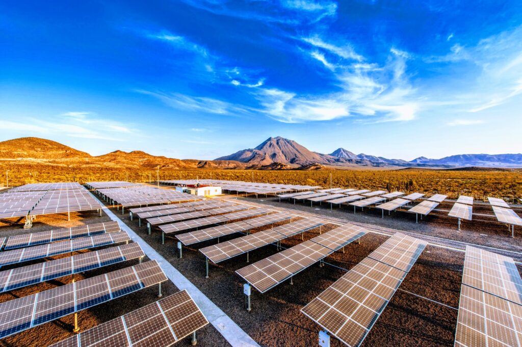 HJ0U4IvXEAAON3d - Petróleo y Energía Rows of solar panels in a desert solar farm with a blue sky and distant mountains on the horizon.