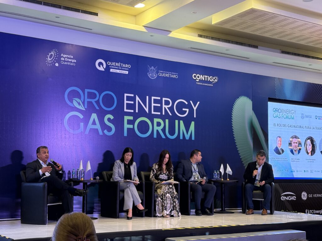 - Petróleo y Energía Panel of seven professionals seated on a stage during a QRO Energy Gas Forum discussion, with a blue backdrop and logos behind them.