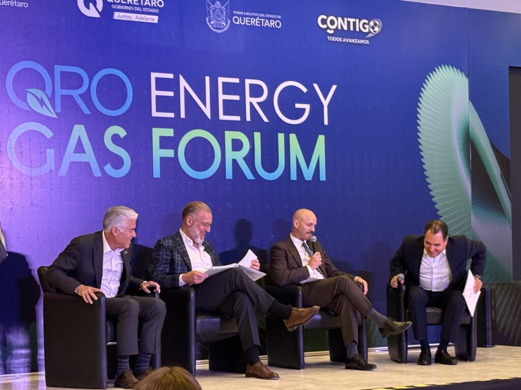 - Petróleo y Energía Panel discussion at the Energy Gas Forum with five men in suits seated on stage against a blue backdrop bearing event logos and text.