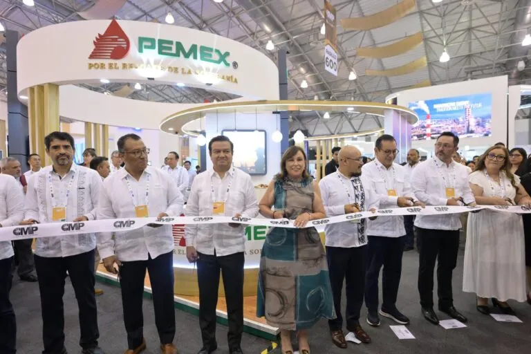 Group of professionals at a trade show ribbon-cutting, in front of a Pemex booth with a curved white display and yellow lighting.