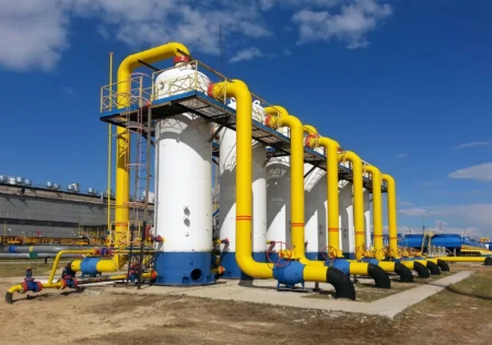Industrial plant with large white storage tanks and bright yellow pipelines against a clear blue sky