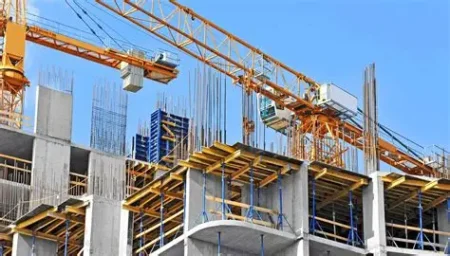 Orange construction crane above a multi-story concrete building under construction against a blue sky, with visible formwork and scaffolding.