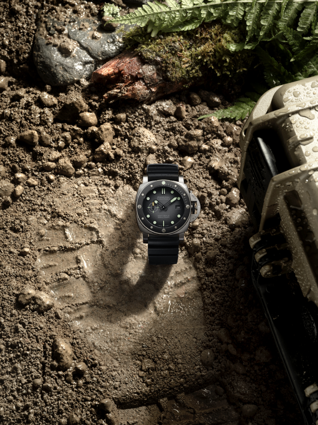PANERAI 2 - Petróleo y Energía Diving watch with black dial and rubber strap lies in wet dirt beside a muddy vehicle, fern in the background.
