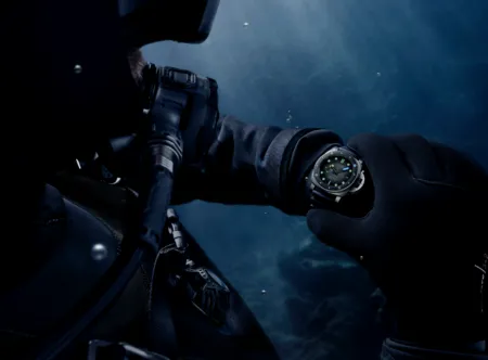 Diver in a wetsuit underwater, with a rugged wristwatch visible on the left wrist.