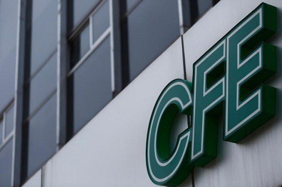 Close-up of a green 3D CFE sign mounted on a white wall beside a glass-fronted building