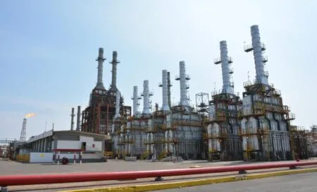 Industrial oil refinery complex with multiple tall distillation towers and yellow safety railings under a clear blue sky