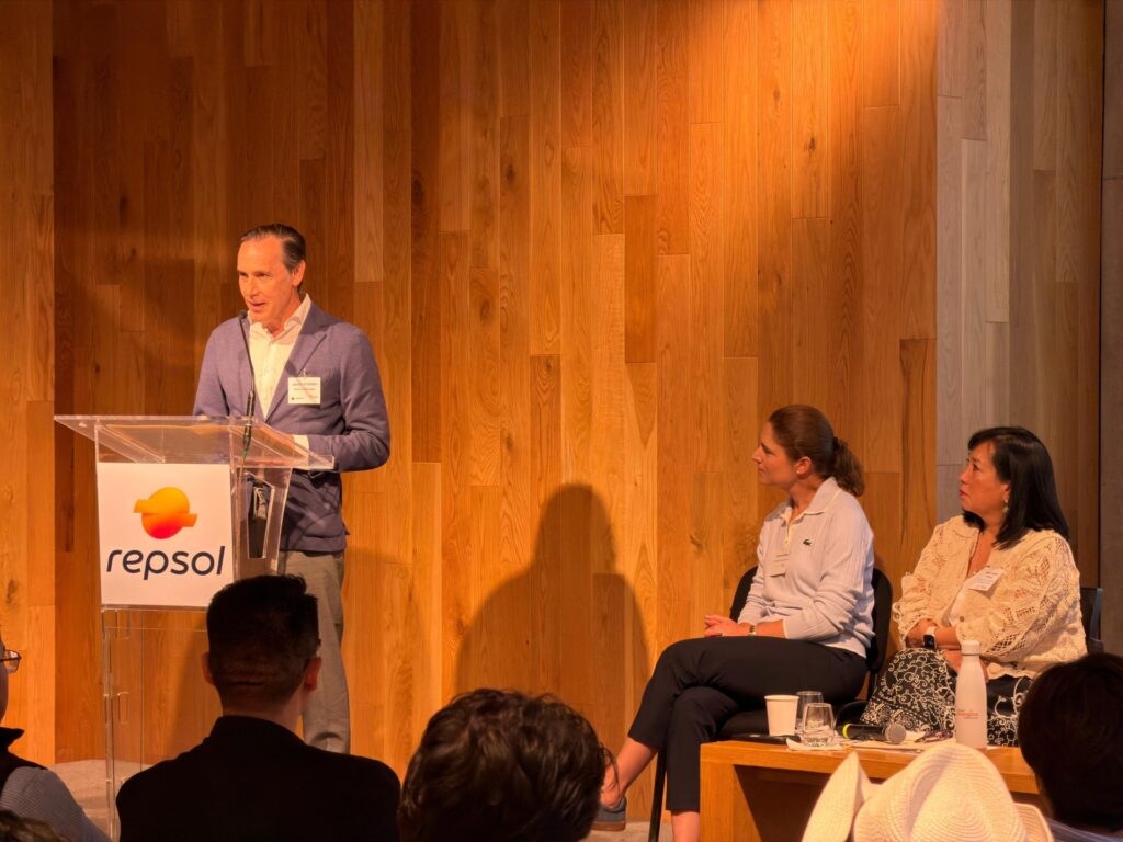 Repsol Energiza mi Proyecto Jesus Chillon 2026jpg - Petróleo y Energía Man in a blue blazer speaks at a transparent lectern with a Repsol logo; three panelists sit to his right against a wooden paneled backdrop.