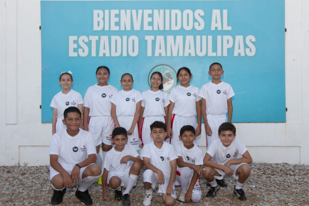 WOODSIDE CAMPEON DE CAMPEONES 1 - Petróleo y Energía Group of children in white sports uniforms posing on steps against a blue sign reading Bienvenidos al Estadio Tamaulipas.
