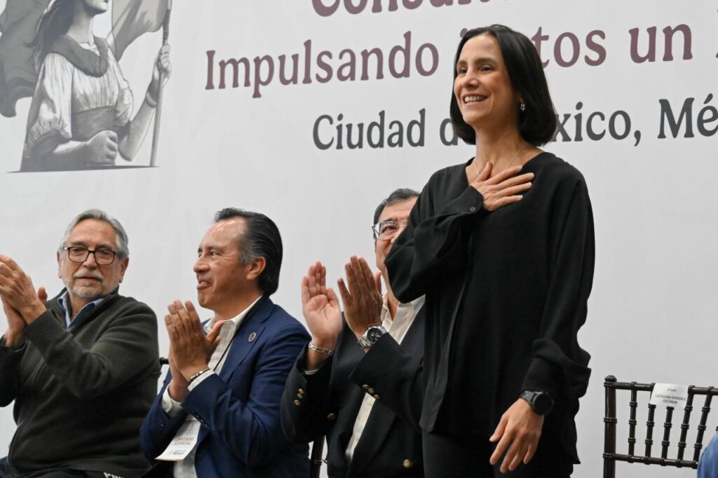 WhatsApp Image 2026-06-05 at 94852 AM 1 - Petróleo y Energía Smiling woman in black stands while three men applaud on a stage at a formal event in Mexico City backdrop.