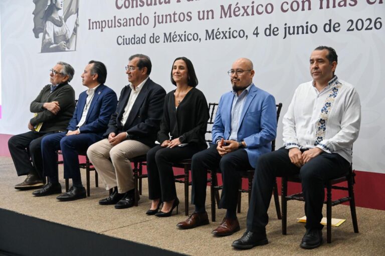 Six people seated in a row on a stage at a formal event in Mexico City, with a Spanish banner behind them.