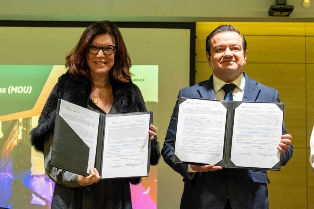 Two professionals in formal attire display signed documents during a signing ceremony, smiling at the camera.