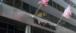Modern office building with a BlackRock sign and two waving American flags on tall flagpoles.