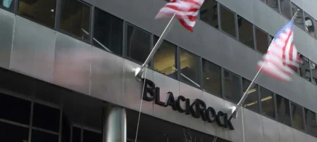 Modern office building with a BlackRock sign and two waving American flags on tall flagpoles.