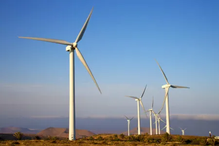 Wind turbines standing in a desert valley under a clear blue sky with distant mountains on the horizon.