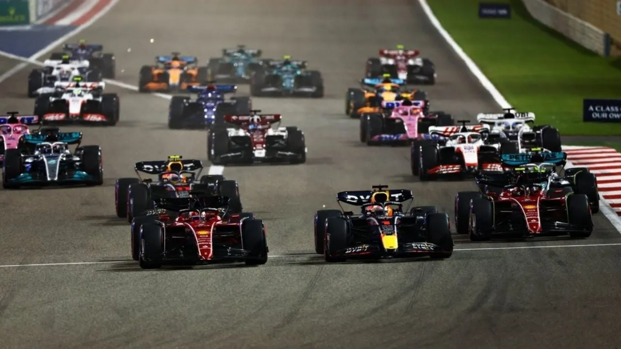 A pack of Formula 1 cars accelerates from the start on a race track, with red Ferraris at the front.