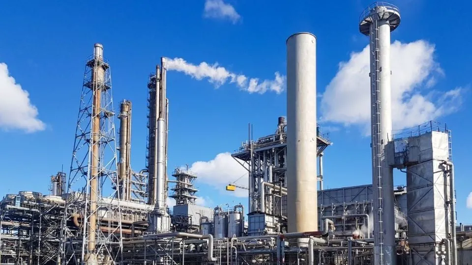 Industrial refinery with tall processing towers and interconnected pipes against a blue sky.