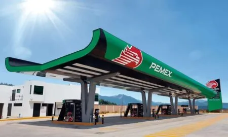 Pemex gas station canopy with green roof and red logo, multiple fuel pumps under a modern structure on a sunny day