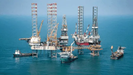Offshore oil drilling platform with multiple derricks and support vessels in a calm blue sea.