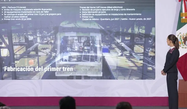 Woman presenting on stage beside a large slide titled 'Fabricación del primer tren' with bullet points visible on screen.