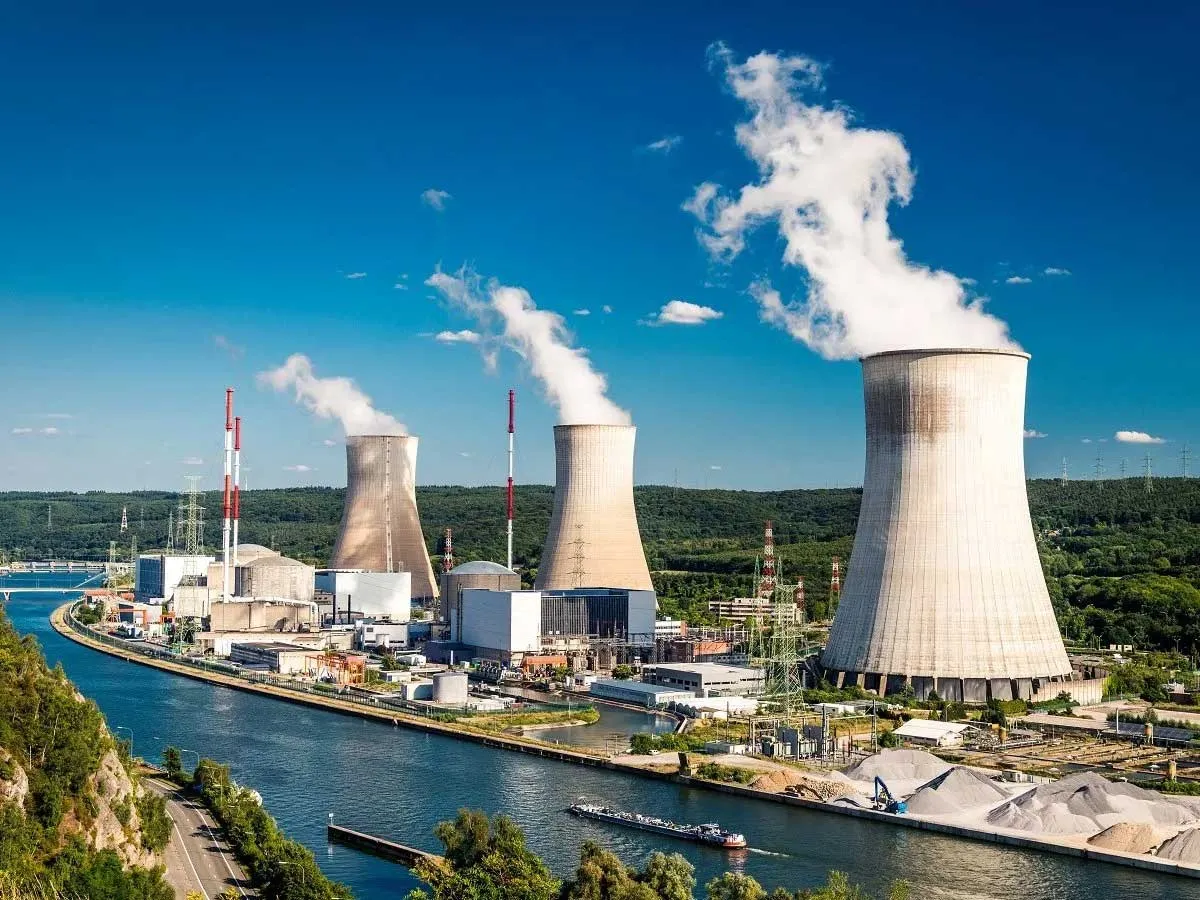 Large power plant with four cooling towers releasing steam beside a river.