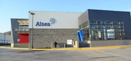 Modern commercial building with the Alsea sign on a light gray wall and a clear blue sky behind it.