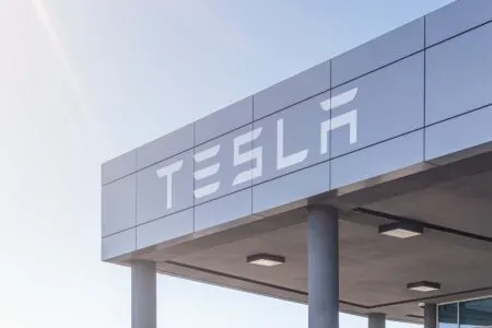 Tesla sign on a modern building canopy with a metallic panel facade and blue sky behind