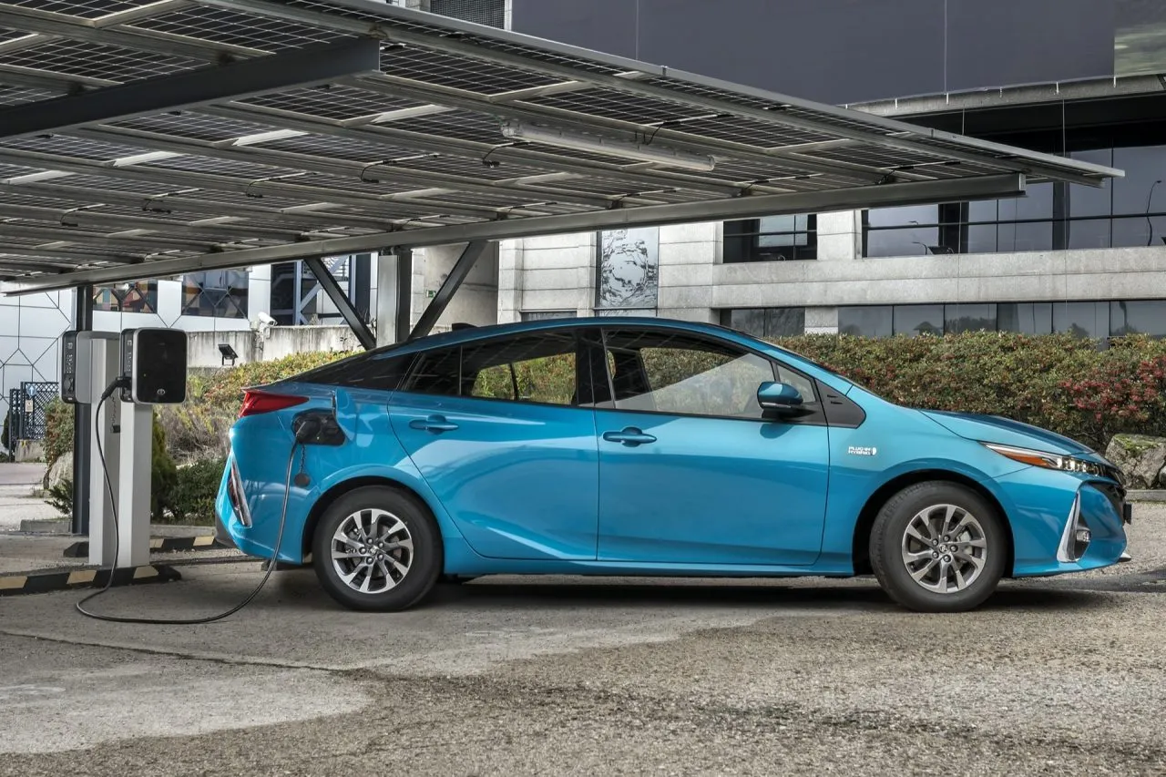Blue electric sedan plugged into a public charging station under a metal canopy.
