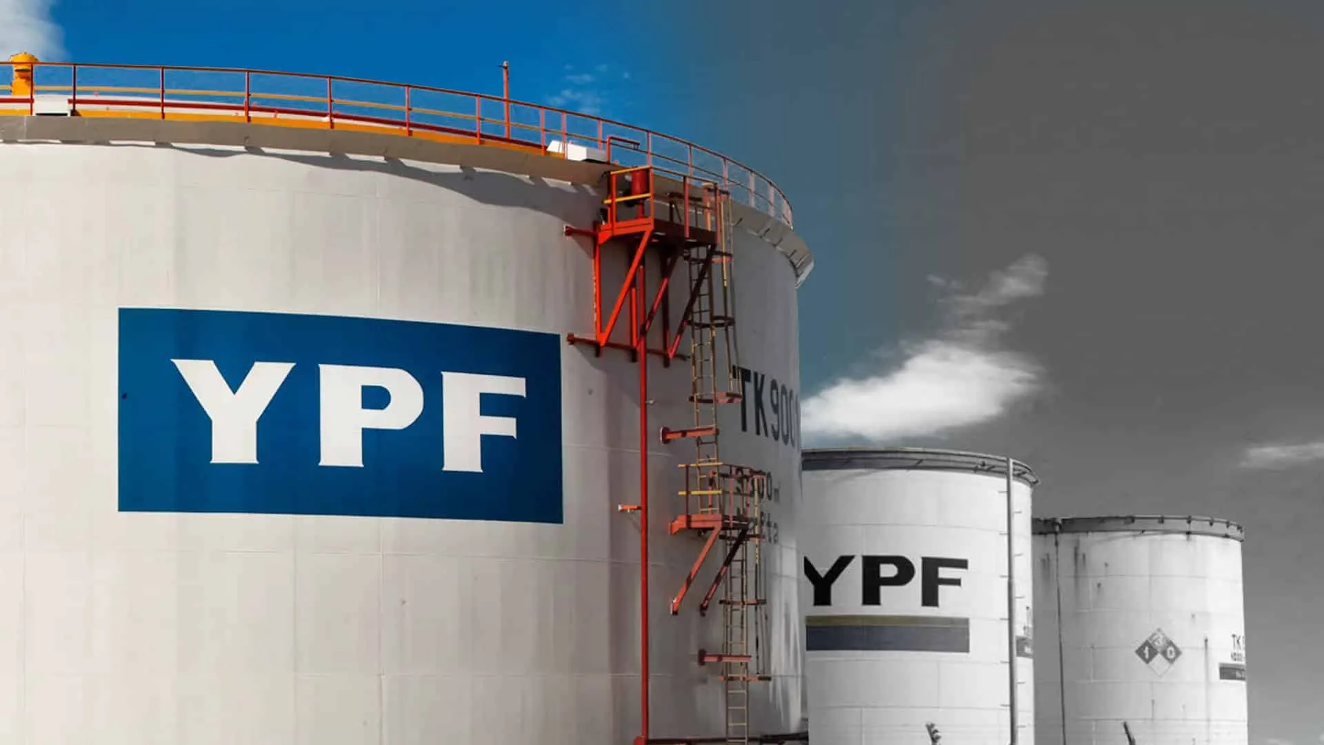 Large white YPF storage tanks with red exterior ladders against a blue sky.