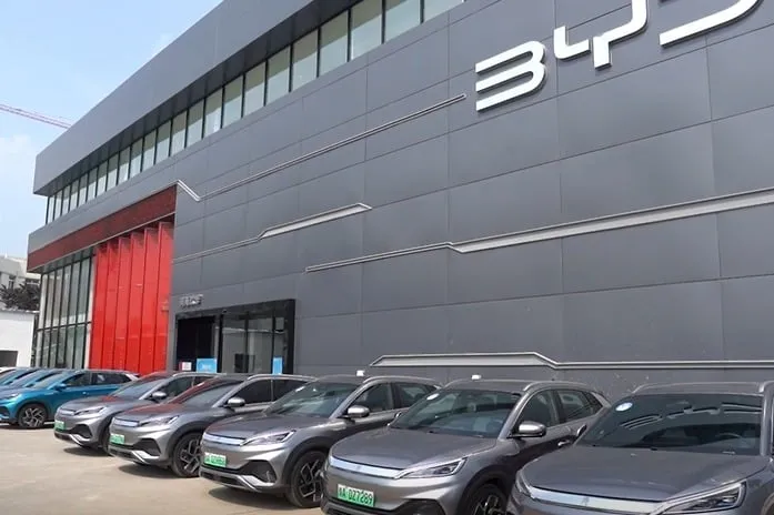 Line of new BYD sedans parked outside a modern showroom with a large BYD logo on the building.