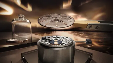 Close-up of a disassembled luxury watch movement on a workbench with a glass cloche nearby, in a warm workshop setting.