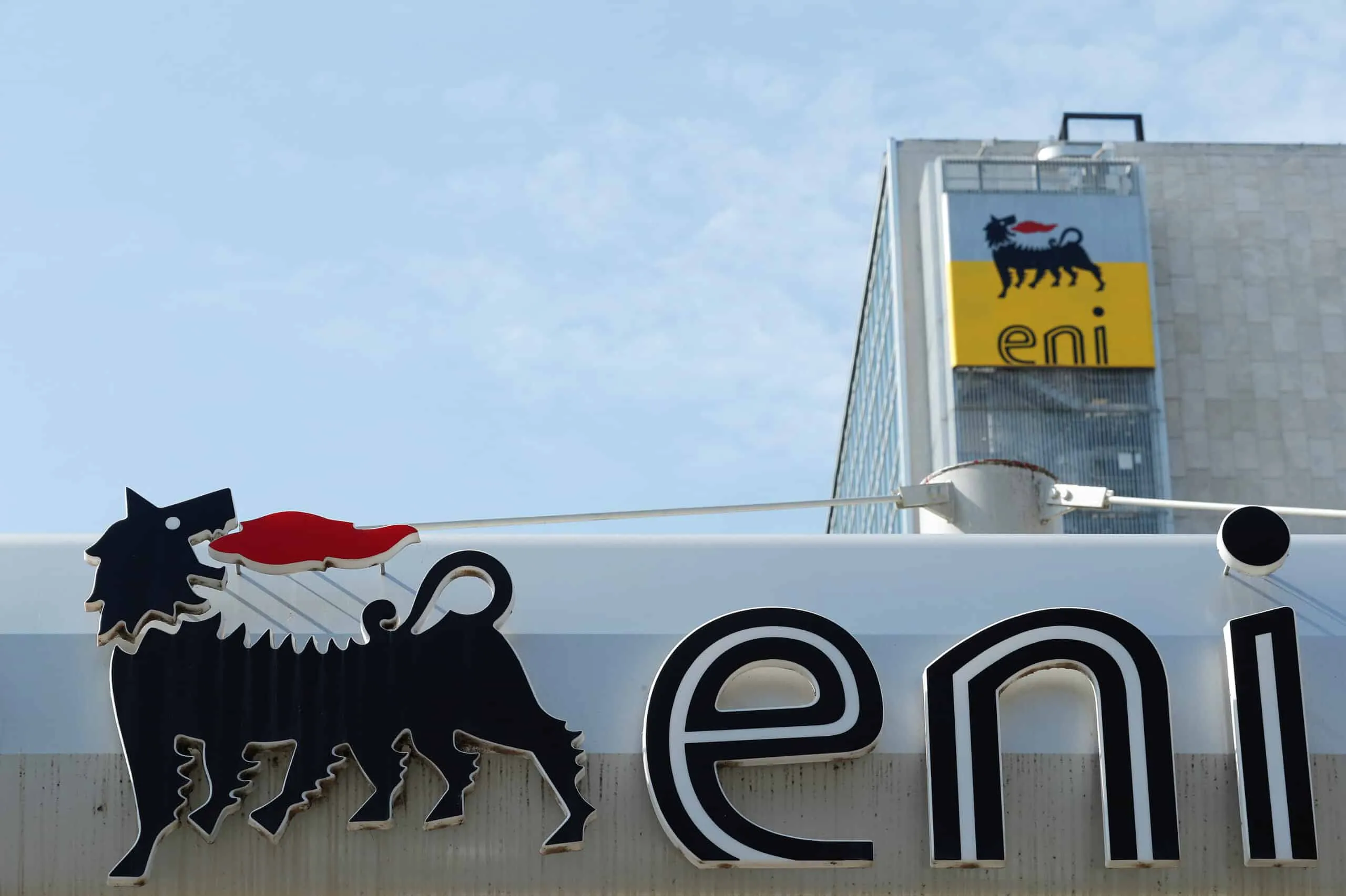Partial view of a building sign showing the ENI logo—the black dog on a yellow background—against a blue sky.