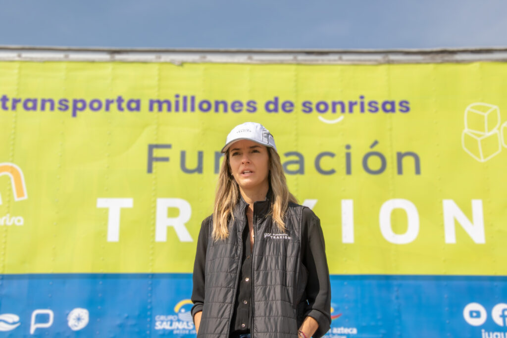 Alejandra Méndez_G4A8650 - Petróleo y Energía Woman in a dark quilted vest and white cap standing in front of a bright yellow banner with Spanish text behind her