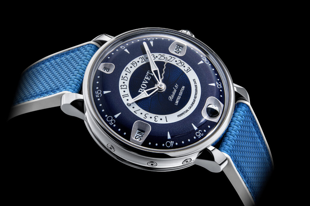 BV_THE RÉCITAL 31_PRODUCT PHOTO BLACK 3 - Petróleo y Energía Close-up of a blue dial wristwatch with a blue woven strap and silver case, showing date and day indicators.