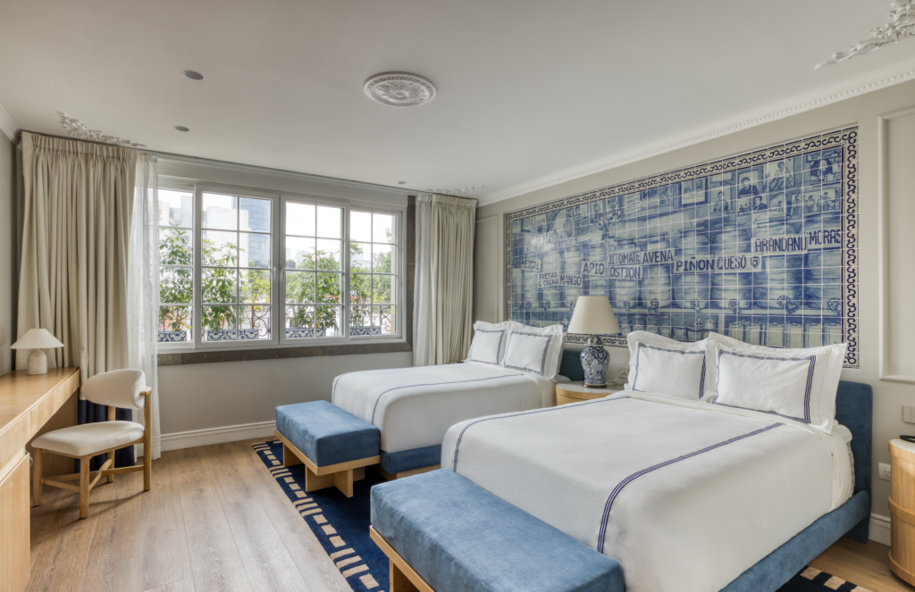 CASA TALAVERA 2 - Petróleo y Energía Hotel bedroom with two twin beds, white bedding, and blue tufted benches at the foot of each bed; a large blue azulejo mural runs along the wall behind the beds.