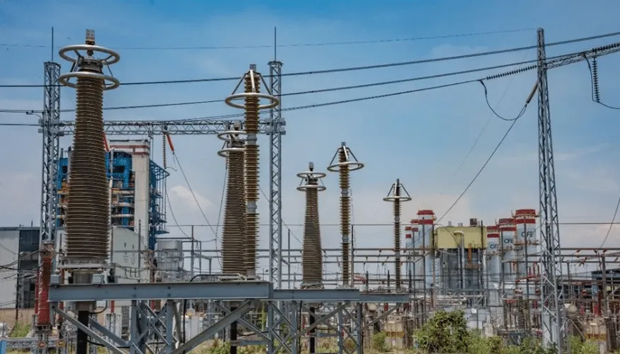 Row of tall ceramic insulators on a high-voltage substation against a blue sky.