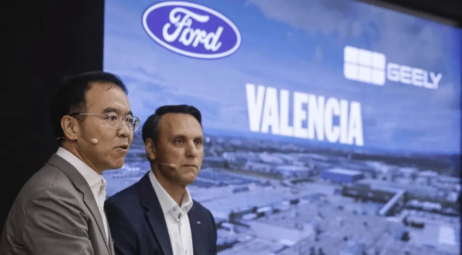 Two men in suits give a talk on stage with headset mics, in front of a large screen showing Ford, Geely logos and the word VALENCIA.