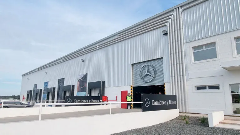 Exterior view of a Mercedes-Benz facility with a large emblem above a garage door and banners along the front, indicating a truck and bus center (Camiones y Buses).