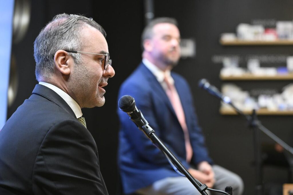 Eugenio Grandio Presidente de la EMA - Petróleo y Energía Man in a dark suit and glasses speaks into a microphone during a panel, with a second speaker in a blue suit blurred in the background.