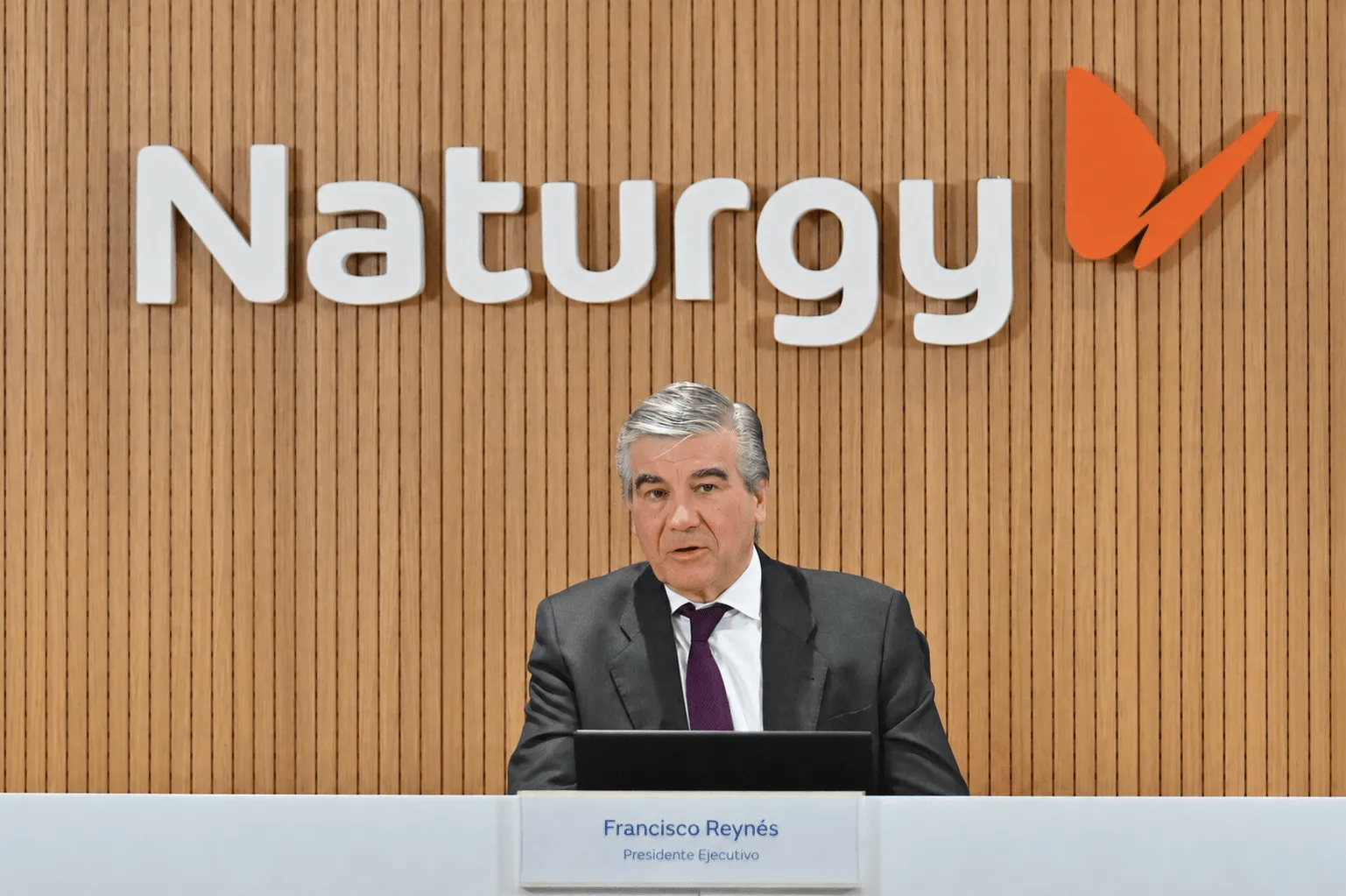 Francisco Reynés, executive president, speaking at a Naturgy press conference behind a wood-paneled wall with the Naturgy logo