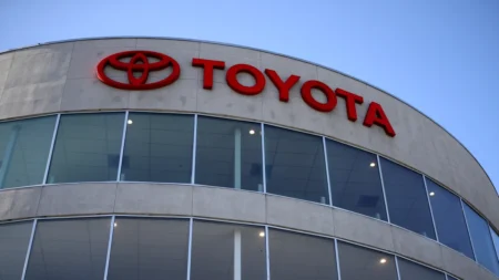 Toyota dealership building with red logo and 'TOYOTA' signage on curved glass facade against a blue sky.