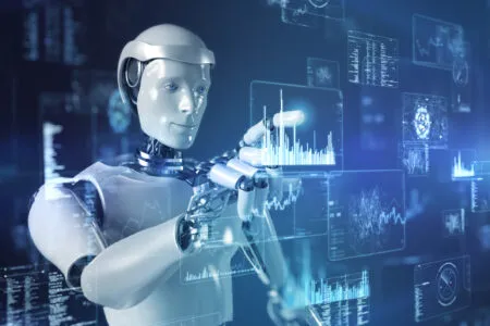 Humanoid robot touches a holographic data dashboard with blue charts and graphs in a high-tech setting.