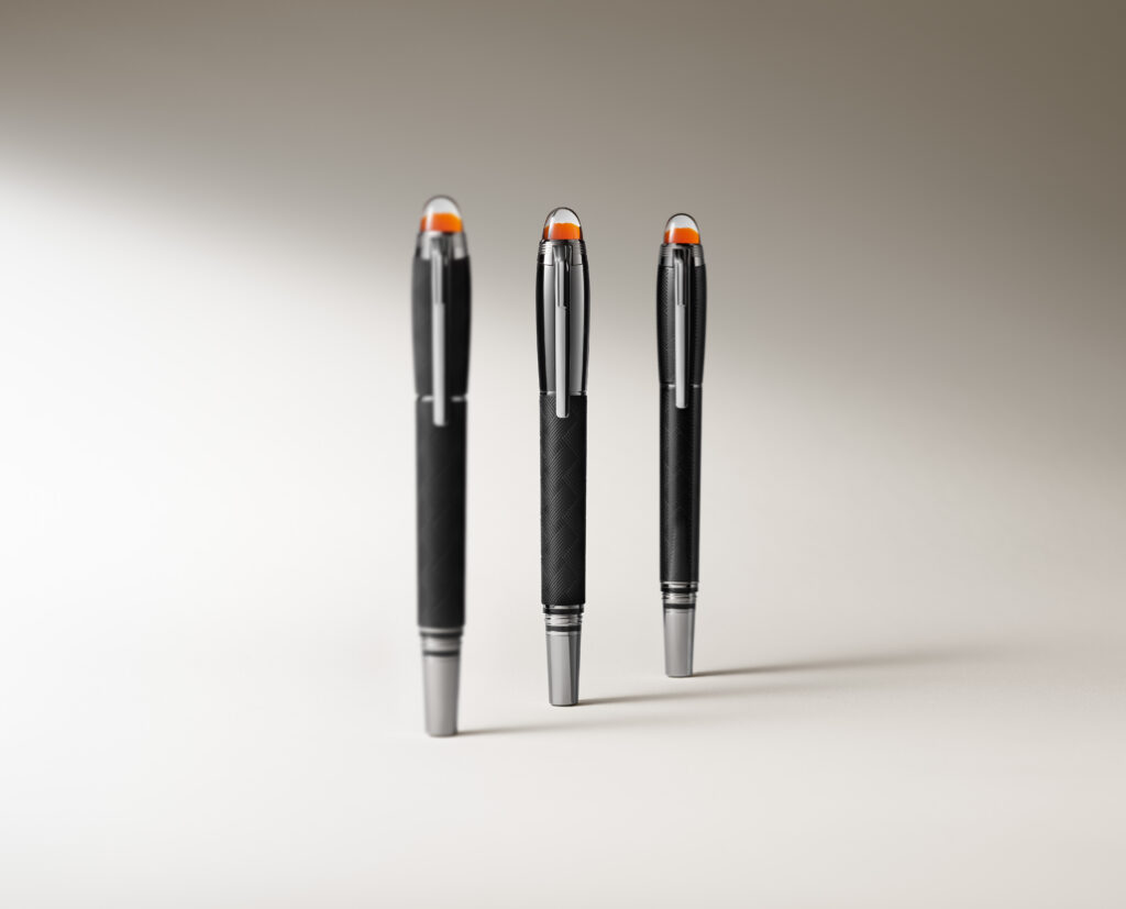 Group Shot - Editorial 2 - Petróleo y Energía Three black pens with orange caps stand upright on a white surface, close to the camera lens in a shallow-depth photo.